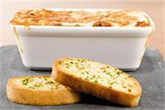 oven dish filled with lasagne, placed on a slate alongside two pieces of garlic bread 