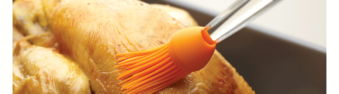 orange silicone pastry brush brushing a cooked chicken 