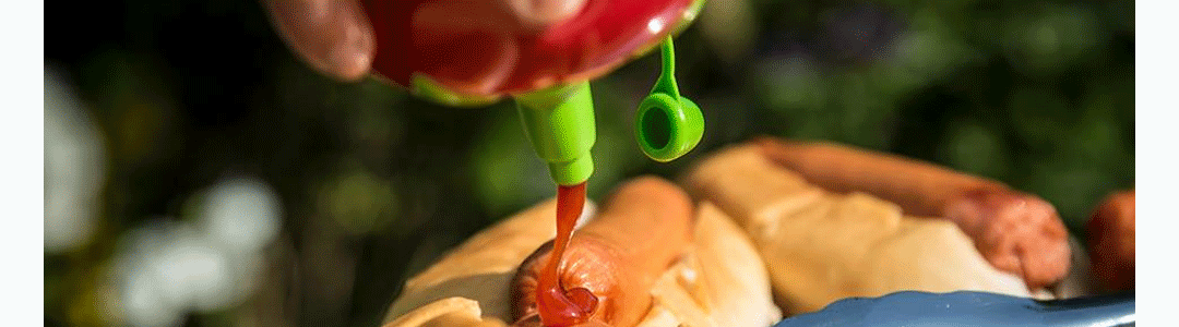 a sauce bottle squeezing ketchup on to a got dog 