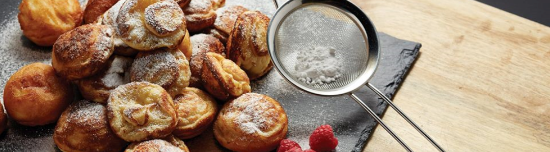 sieve filled with icing sugar accompanied by pastries and raspberries on a slate board
