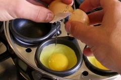 egg being cracked into an egg poacher