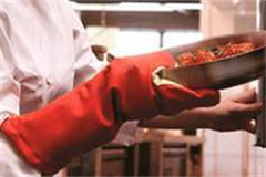 chef wearing oven gloves putting pan into oven 