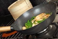 wok on a stove containing chicken and various vegetables