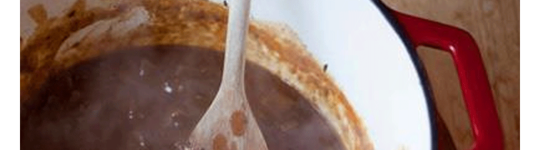 cast iron casserole dish full of casserole being mixed with a wooden spoon