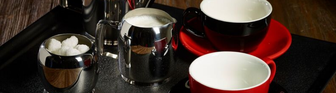 stainless steel milk jug containing milk on a tray with tea cups 