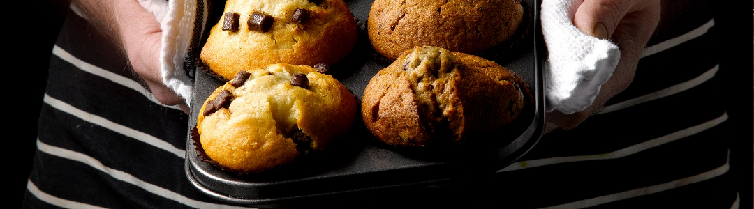 man holding muffin pan with four baked muffins