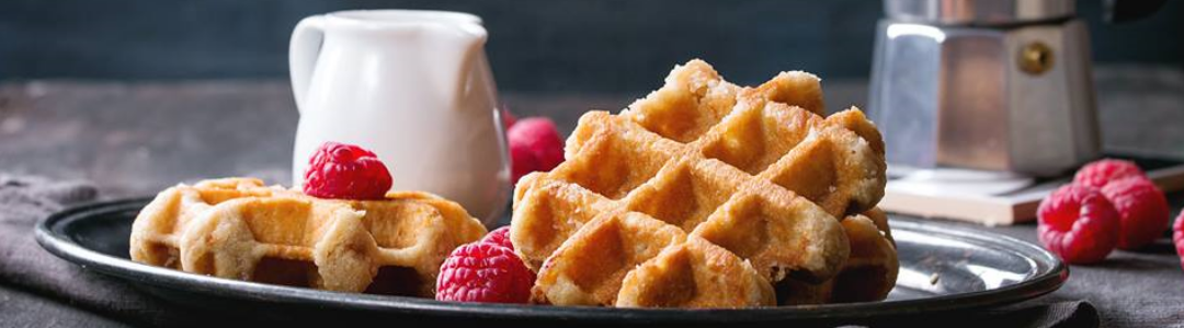 two waffles, with raspberries and jug of cream on plate